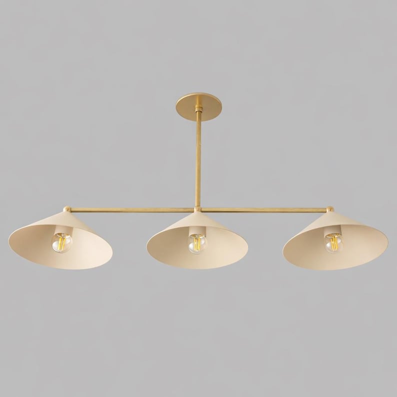 A three-light linear chandelier featuring a central brass rod and a horizontal bar supporting three cone-shaped shades in a matte cream finish. Each shade houses a single exposed light bulb, creating a balanced and symmetrical fixture.