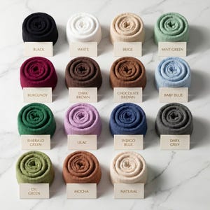 May include: A collection of sixteen rolled blankets in various colors, including black, white, beige, mint green, burgundy, dark brown, chocolate brown, baby blue, emerald green, lilac, indigo blue, dark grey, oil green, mocha, and natural.