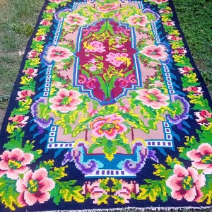 Peut inclure: Un tapis rectangulaire orné d'un motif floral vibrant avec des fleurs roses, jaunes et vertes sur un fond noir profond. Le design central comprend un médaillon bordeaux entouré de bordures marron clair et d'accents géométriques.
