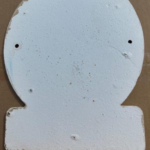 Puede incluir: Un letrero de metal blanco en forma de campana con un acabado texturizado y desgastado. El letrero presenta una secci&oacute;n superior redondeada y una base rectangular, con dos orificios de montaje circulares colocados sim&eacute;tricamente en la mitad superior.