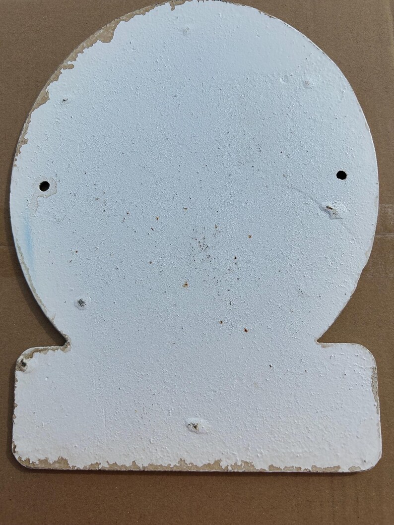 Puede incluir: Un letrero de metal blanco en forma de campana con un acabado texturizado y desgastado. El letrero presenta una secci&oacute;n superior redondeada y una base rectangular, con dos orificios de montaje circulares colocados sim&eacute;tricamente en la mitad superior.
