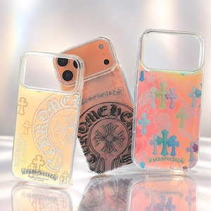 Puede incluir: Tres fundas transparentes para teléfono con la marca Chrome Hearts. La funda izquierda tiene un tono amarillo con un logotipo circular. La central es naranja con un gran emblema negro. La derecha tiene un fondo multicolor con pequeñas cruces.
