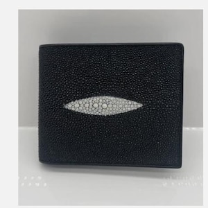Peut inclure: Portefeuille en cuir noir avec un motif de raie manta blanc au centre. Le portefeuille a une surface texturée et une forme rectangulaire. Le motif de raie manta est ovale et présente un motif de petits cercles blancs.