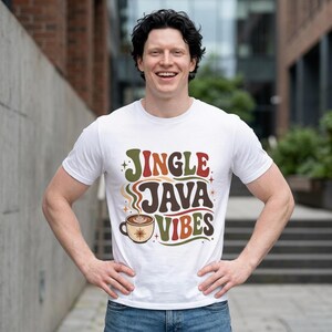 May include: A white short-sleeved t-shirt featuring a graphic print with the text JINGLE JAVA VIBES in retro-style brown, green, and orange lettering, accompanied by an illustration of a coffee cup with steam and small star accents.