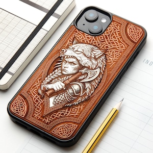 Pode incluir: Uma capa de telemóvel retangular com moldura preta e painel traseiro em tom de madeira castanha. A parte de trás apresenta um design intrincado gravado a laser de uma pessoa com um toucado de lobo e um machado, rodeado por nós celtas detalhados.