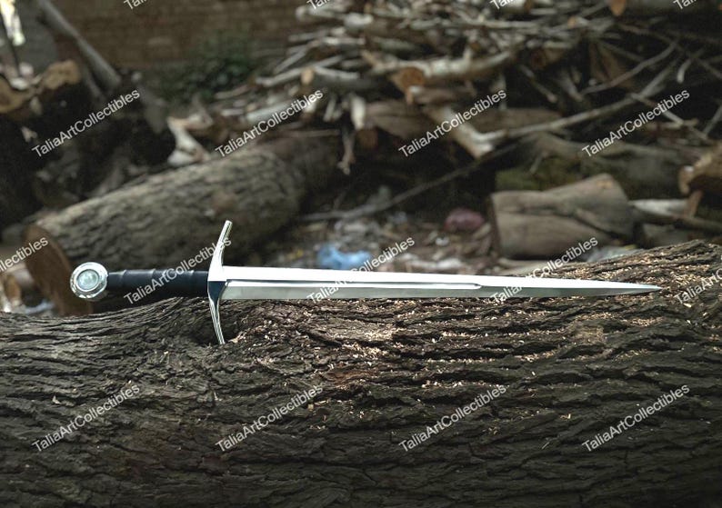 May include: A silver and black sword with a crossguard and a rounded pommel, resting on a textured, brown log. The blade is polished and reflects light. The sword's handle is black, and the crossguard is silver.
