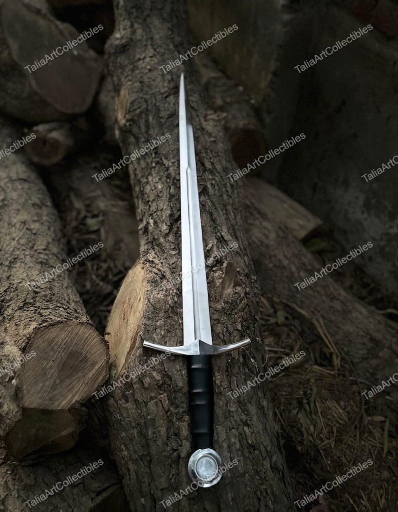 May include: A silver sword with a black handle and a crossguard. The sword is resting against a tree trunk. The blade is long and sharp, and the handle is wrapped in black material. The crossguard is silver and has a simple design.