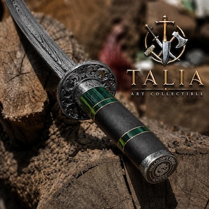 May include: A dagger with a dark Damascus steel blade, a circular ornate guard, and a black handle featuring green striped accents. The pommel is engraved with the text "DRAGON'S EDGE KNIVES". The image includes the logo "TALIA ART COLLECTIBLE".