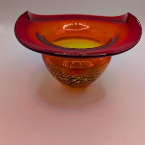 May include: A glass bowl featuring a vibrant red rim that transitions into a bright orange center. The exterior of the bowl displays a distinct crackle texture throughout the glass, while the interior remains smooth with a wide, flared opening.