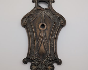 Placa de puerta de bronce antiguo con herrajes y diseño de corona ornamentada.