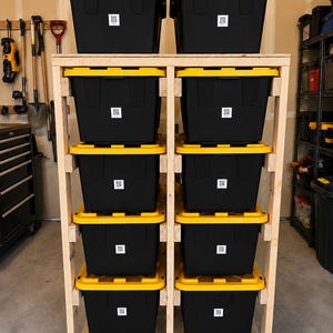 May include: A tall, light-colored wooden storage rack on wheels, featuring two vertical columns. It holds ten black plastic storage bins with bright yellow lids. Each bin is marked with a small, square white label containing a black QR code.