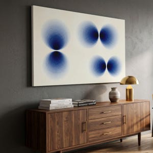 Puede incluir: Un gran lienzo rectangular con seis diseños de círculos concéntricos azules sobre un fondo blanco. La obra de arte cuelga sobre un mueble de madera con cajones y puertas. Una lámpara dorada y un jarrón están sobre el mueble.