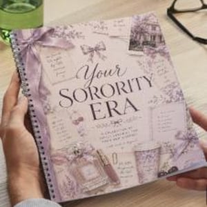 Pode incluir: Um caderno espiralado com o texto "Your Sorority Era" em escrita elegante. A capa apresenta um esquema de cores lavanda e creme com laços decorativos, frascos de perfume e esboços arquitetônicos. Uma caneta repousa na capa.