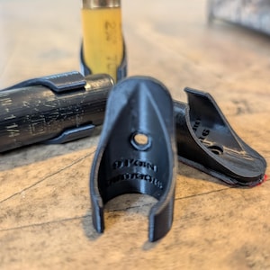 May include: A set of black 3D-printed plastic shotgun shell holders with a curved, open-ended design. Each holder features a central mounting hole and the embossed text 9 POINT OUTDOORS on the interior surface, designed to clip onto shells.