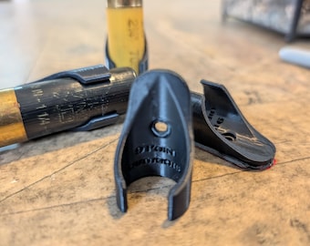 Könnte beinhalten: Ein Set aus schwarzen, 3D-gedruckten Kunststoffhaltern für Schrotpatronen mit gebogenem, offenem Design. Jeder Halter verfügt über ein zentrales Montageloch und den geprägten Schriftzug 9 POINT OUTDOORS auf der Innenseite zur Befestigung.