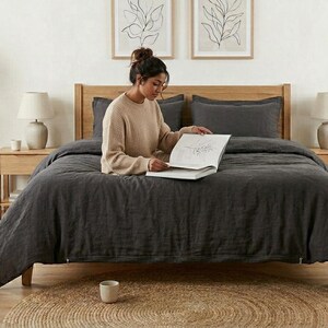 Charcoal gray linen bedding set on a wooden bed in a bright minimalist bedroom, featuring soft washed linen texture, neutral decor, natural light, and modern Scandinavian styling.