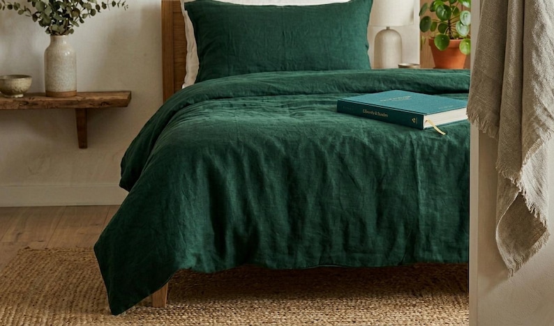 Dark emerald green linen bedding set on a wooden bed in a minimalist bedroom with natural wood furniture, soft neutral decor, and warm natural light.