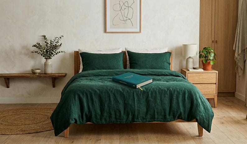 Dark emerald green linen bedding set on a wooden bed in a minimalist bedroom with natural wood furniture, soft neutral decor, and warm natural light.