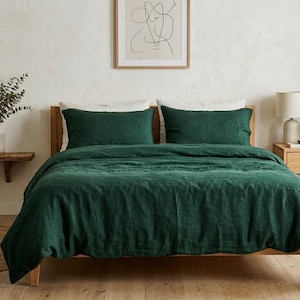 Dark emerald green linen bedding set on a wooden bed in a minimalist bedroom with natural wood furniture, soft neutral decor, and warm natural light.