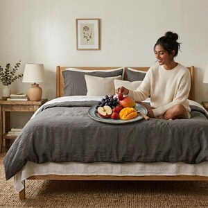 Charcoal gray linen bedding set on a wooden bed in a bright minimalist bedroom, featuring soft washed linen texture, neutral decor, natural light, and modern Scandinavian styling.