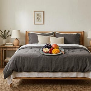 Charcoal gray linen bedding set on a wooden bed in a bright minimalist bedroom, featuring soft washed linen texture, neutral decor, natural light, and modern Scandinavian styling.