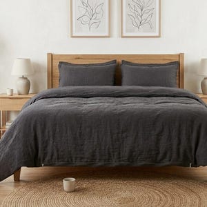 Charcoal gray linen bedding set on a wooden bed in a bright minimalist bedroom, featuring soft washed linen texture, neutral decor, natural light, and modern Scandinavian styling.
