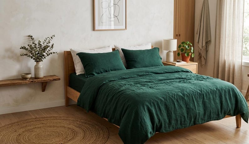 Dark emerald green linen bedding set on a wooden bed in a minimalist bedroom with natural wood furniture, soft neutral decor, and warm natural light.