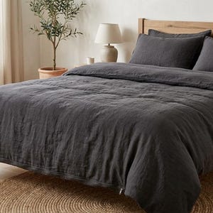 Charcoal gray linen bedding set on a wooden bed in a bright minimalist bedroom, featuring soft washed linen texture, neutral decor, natural light, and modern Scandinavian styling.
