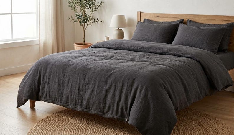 Charcoal gray linen bedding set on a wooden bed in a bright minimalist bedroom, featuring soft washed linen texture, neutral decor, natural light, and modern Scandinavian styling.