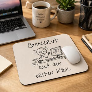 Peut inclure: Un tapis de souris rectangulaire beige avec un dessin au trait noir représentant un personnage bâton frustré devant un ordinateur. Le texte indique "GENervt auf den ersten Klick" avec "KLICK!" près de la souris. Une souris blanche est posée dessus.