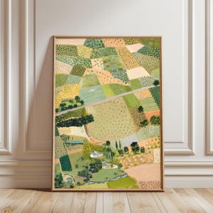 May include: A framed painting of a rural landscape, showing fields in shades of green, yellow, and beige. A road meanders through the fields, and a small village with white buildings is visible. The artwork is presented in a wooden frame.