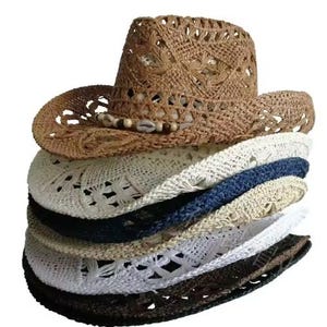 Puede incluir: Una pila de seis sombreros de vaquero de paja trenzada en varios colores, incluyendo bronceado, blanco, azul marino, beige y negro. El sombrero superior presenta una banda decorativa hecha de pequeñas cuentas de madera y conchas blancas.