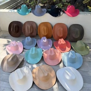 Könnte beinhalten: Eine Sammlung von einundzwanzig Cowboyhüten, die in Reihen angeordnet sind und eine Vielzahl von Unifarben wie Weiß, Schwarz, Rosa, Blau, Braun, Beige, Orange, Grün und Lavendel aufweisen. Jeder Hut hat eine klassische, eingedrückte Krone.