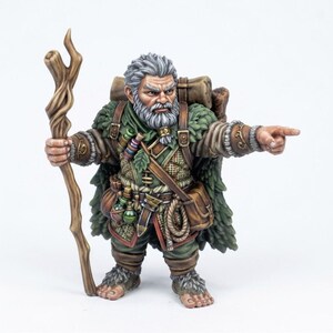 Peut inclure: Une figurine miniature peinte représentant un personnage barbu aux cheveux gris, vêtu d'une cape verte, d'un sac à dos marron et de vêtements texturés. La figurine tient un bâton en bois et pointe le doigt vers l'avant, avec des fioles.