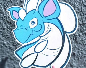 May include: A die-cut vinyl sticker featuring a cartoon dragon with bright blue skin, a white underbelly, and white crests on its head. The dragon has large ears with light purple inner sections and is depicted with a winking expression.