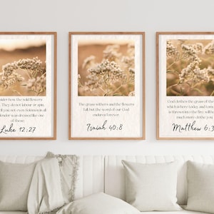 May include: Three framed art prints with botanical photography and Bible verses. Each print features a sepia-toned image of wildflowers and a quote from Luke 12:27, Isaiah 40:8, and Matthew 6:30. The frames are a light brown color.