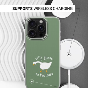以下が含まれることがあります： セージグリーンのスマートフォンケース。白いガチョウのイラストと「silly goose on the loose」という文字が描かれています。ケースには「SUPPORTS WIRELESS CHARGING」および「SIDES ARE NOT PRINTED」というラベルがあり、それぞれの特徴を指し示す線が引かれています。