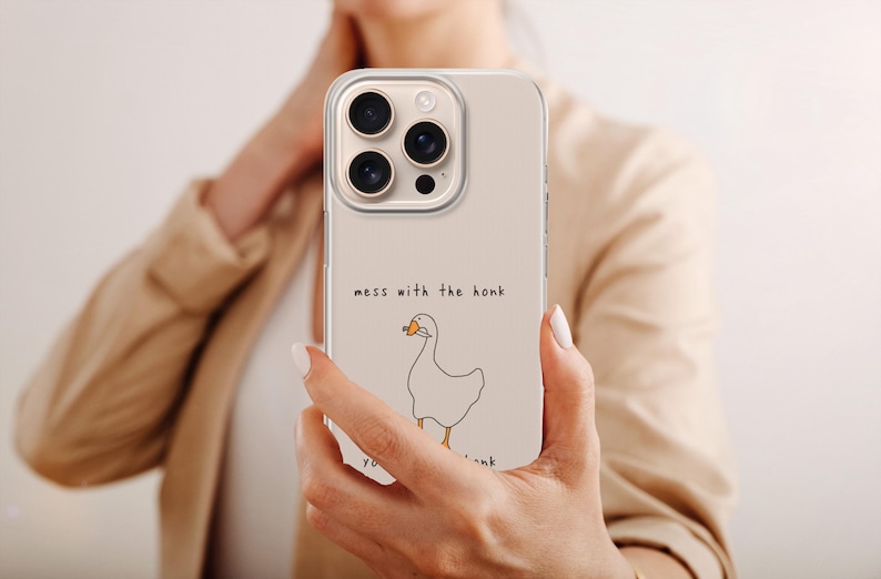 以下が含まれることがあります： オレンジ色のくちばしを持つ白いガチョウのミニマルな線画が描かれたベージュのスマートフォンケース。ガチョウの上にはシンプルな黒いフォントで「mess with the honk」というテキストが印刷されており、ガチョウの下にも部分的なテキストが見えます。