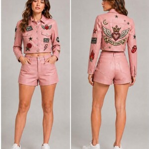 May include: A light pink cropped jacket and matching shorts set. The jacket features a collar, button-down front, and various embroidered patches including a heart, rose, and lightning bolt. The back displays a large winged heart, crown, and text.