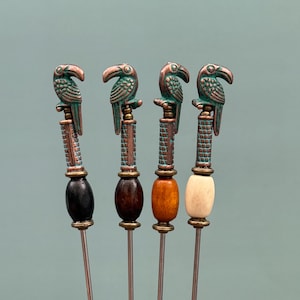 Pode incluir: Quatro palitos de cocktail em metal com um topo de tucano em tom de cobre, um eixo texturizado e uma conta individual. As contas são preta, castanho-escura, castanho-clara e creme. Cada palito tem uma haste de metal prateada longa e fina.