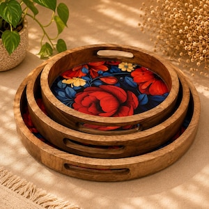 May include: A set of three nested round wooden serving trays with cut-out handles. Each tray features a vibrant floral pattern on the base, displaying large red peonies, smaller yellow blossoms, and dark blue leaves against a deep black background.