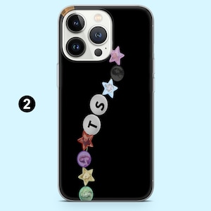 以下が含まれることがあります： 黒い携帯電話ケース、透明な縁取り付き。ケースは、カラフルな星と円形の装飾の垂直デザインが特徴です。「T」、「S」の文字が円に表示されています。電話のカメラレンズが上部に表示されています。