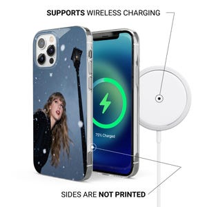 以下が含まれることがあります： 人物と街灯が描かれた冬のシーンが特徴の透明な携帯電話ケース。電話画面には充電シンボルが表示されます。白いワイヤレス充電器も表示されています。画像には「SUPPORTS WIRELESS CHARGING」と「SIDES ARE NOT PRINTED」と書かれています。