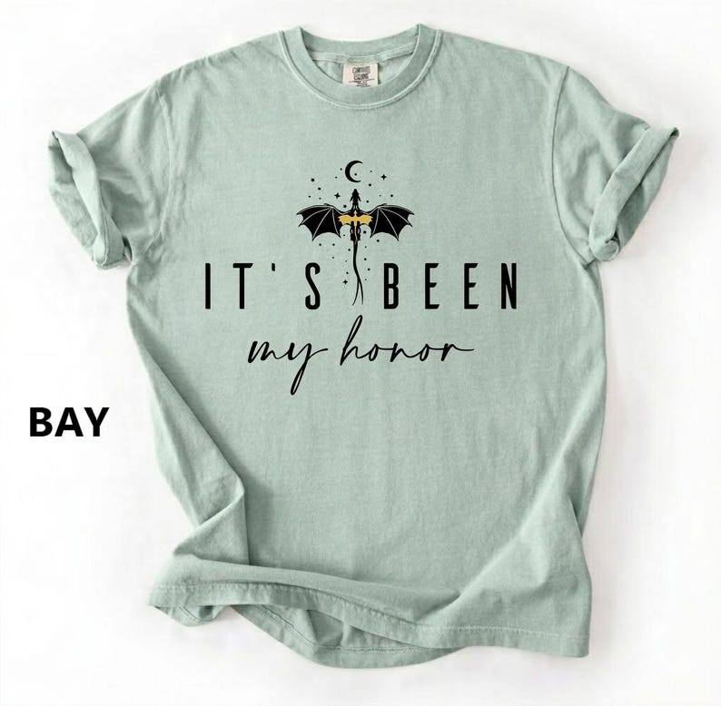 Puede incluir: Camiseta verde claro con el texto negro "IT'S BEEN my honor". Encima, un dibujo de un drag&oacute;n con alas negras y cuerpo amarillo. La palabra "BAY" est&aacute; impresa en la esquina inferior izquierda.