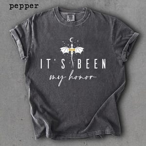 Puede incluir: Camiseta gris oscuro con mangas enrolladas. La camiseta presenta un gr&aacute;fico de drag&oacute;n y el texto "IT'S BEEN my honor" en blanco. La palabra "pepper" est&aacute; en la esquina superior izquierda.