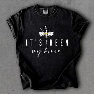 Puede incluir: Camiseta negra con el texto blanco "IT'S BEEN my honor", con un dise&ntilde;o de drag&oacute;n blanco y dorado, con una luna creciente y estrellas encima. La camiseta tiene un aspecto vintage y desgastado.