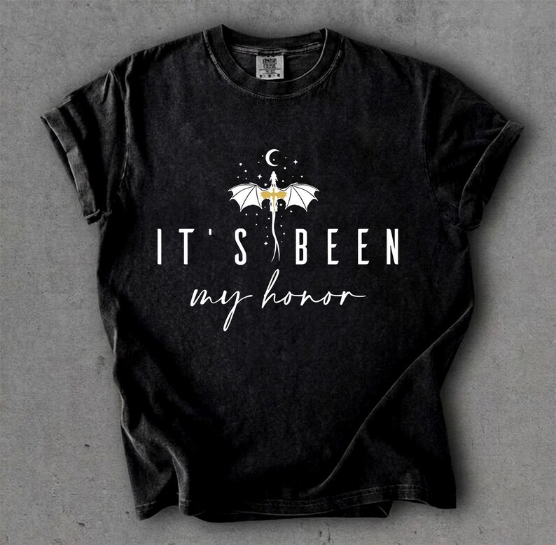 Puede incluir: Camiseta negra con el texto blanco "IT'S BEEN my honor", con un dise&ntilde;o de drag&oacute;n blanco y dorado, con una luna creciente y estrellas encima. La camiseta tiene un aspecto vintage y desgastado.