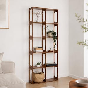 May include: A tall, dark brown wooden bookshelf with multiple cubby shelves and vertical cutouts. The shelves are filled with decorative items, including plants, books, and a woven basket. The bookshelf is against a white wall.