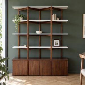 May include: A tall shelving unit featuring a dark wood base with four cabinet doors and a frame of dark wood vertical supports. It includes five horizontal white shelves holding a potted trailing plant, books, a white bowl, and a framed picture.