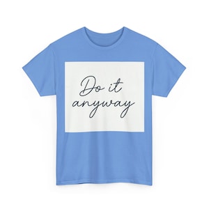 Può includere: Una t-shirt a maniche corte di colore azzurro con un riquadro bianco centrato sul petto. All'interno del riquadro bianco, il testo "Do it anyway" è stampato in un carattere nero corsivo in stile calligrafico. La maglia ha un girocollo.